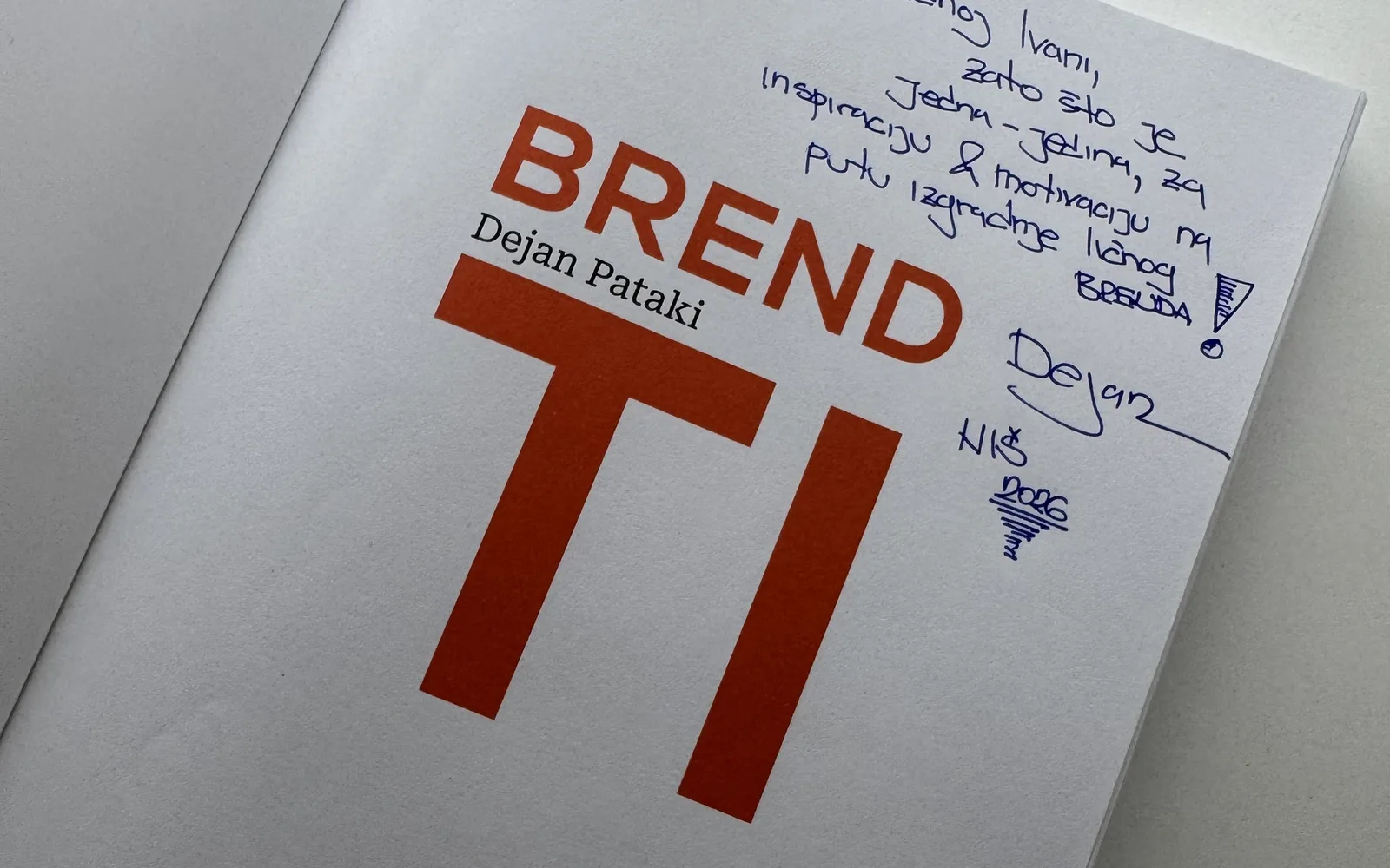 Otvorena knjiga „Brend ti” Dejana Patakija sa posvetom, na stolu.